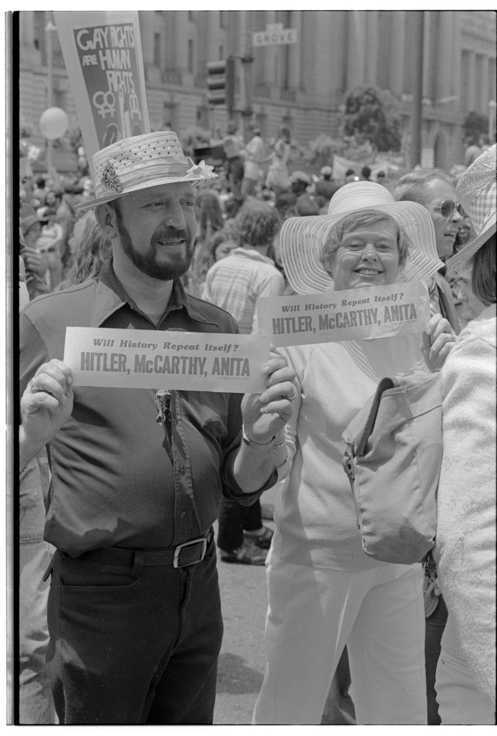 Men and women participating in the San Francisco Gay Freedom Day parade hold up bumper stickers with the words 