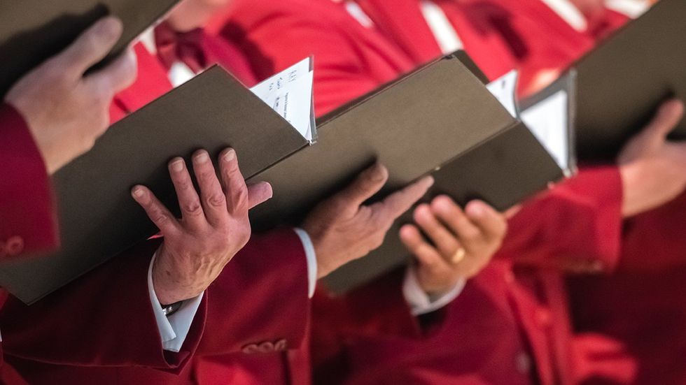 Close up of mens choir members holding singing book while performing in a cathedral