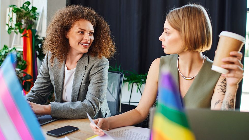 coworkers talking about being out at work LGBTQ rainbow flag transgender pride flag on desk