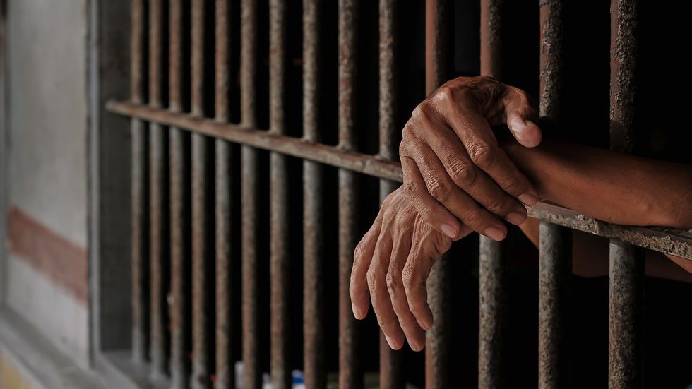 Man's hands extending through prison bars