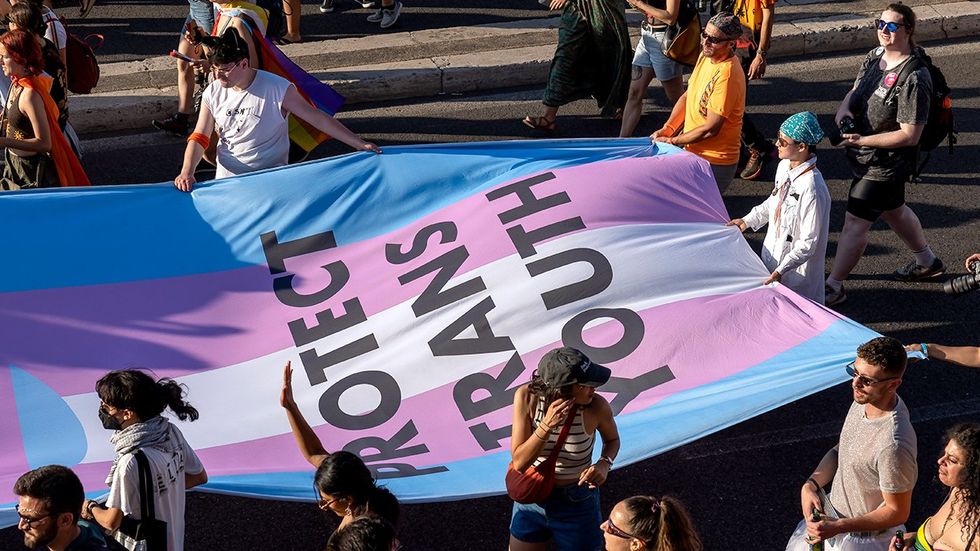 marchers holding giant transgender flag says protect trans youth LGBTQIA pride parade from above