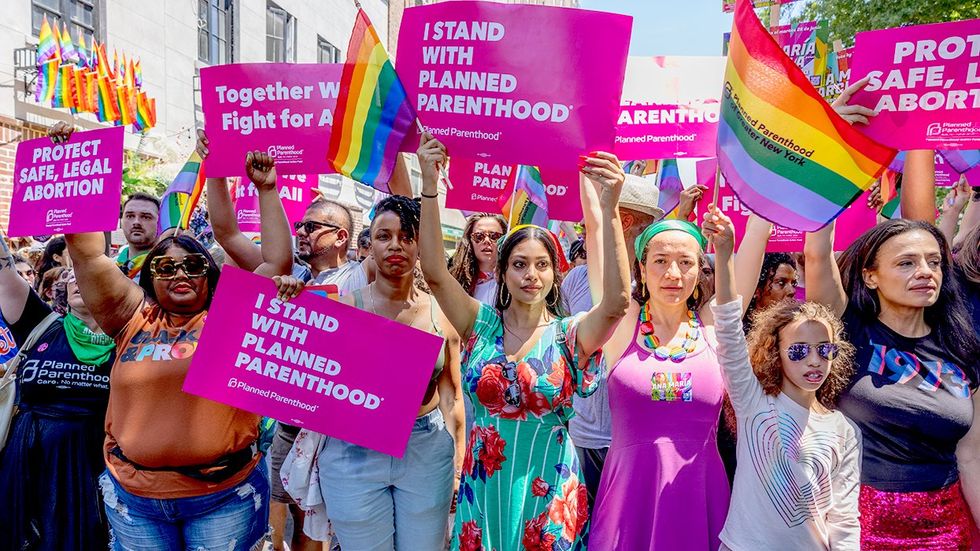 people holding stand with planned parenthood signs rainbow flags NYC LGBTQ pride march outside stonewall inn bar