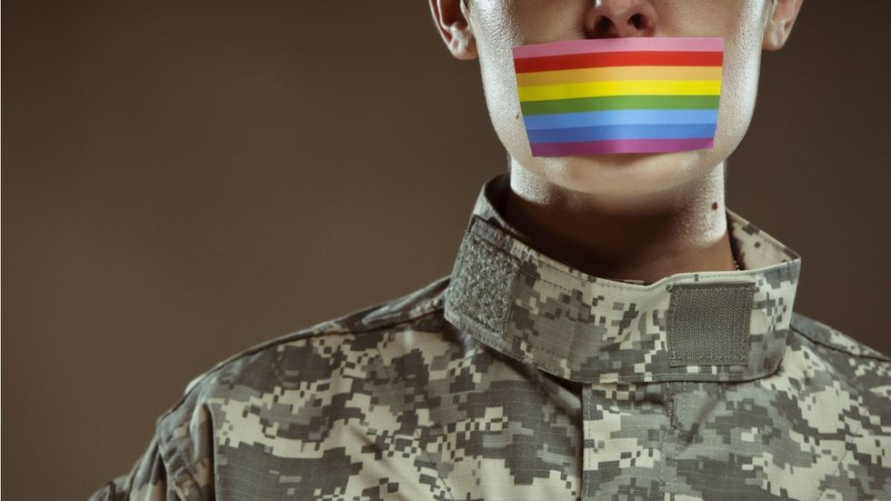 Person in military clothes with rainbow card over their mouth