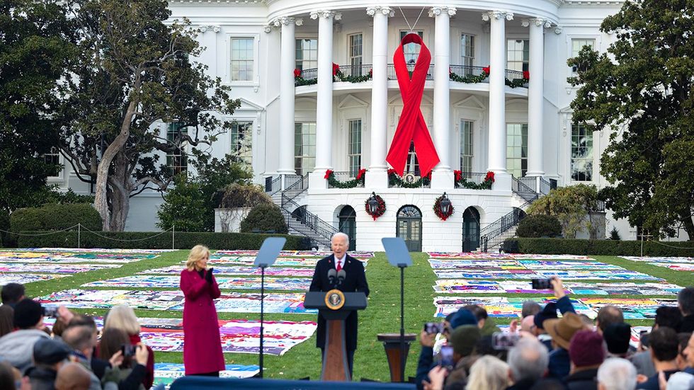 President Joe Biden speaks at a ceremony on the White House South Lawn commemorating World AIDS Day 2024 Red Ribbon and memorial quilt panels in background