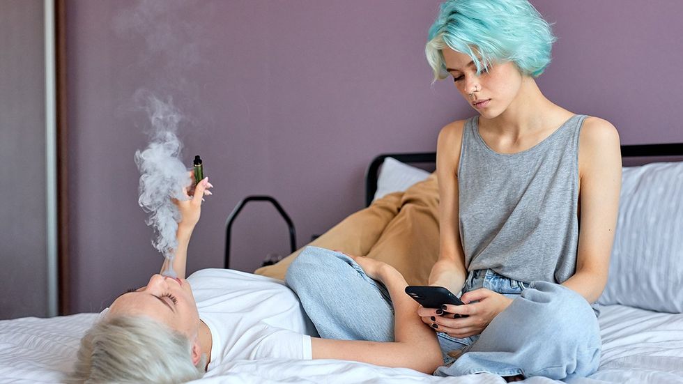 queer sapphic couple lesbians in bed one vaping one reading cell phone