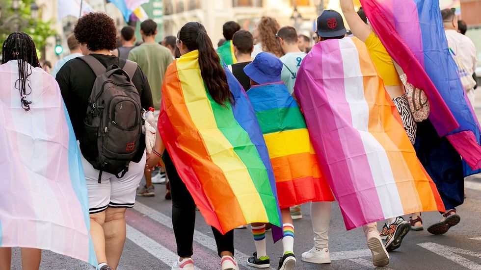 rainbow flag capes pride parade queer youth walking in the street celebrating LGBTQ rights