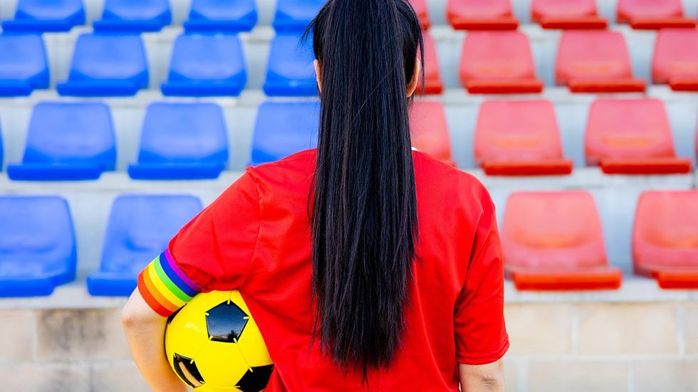 Soccer player holding ball LGBTQ rainbow pride flag armband red blue stadium seats