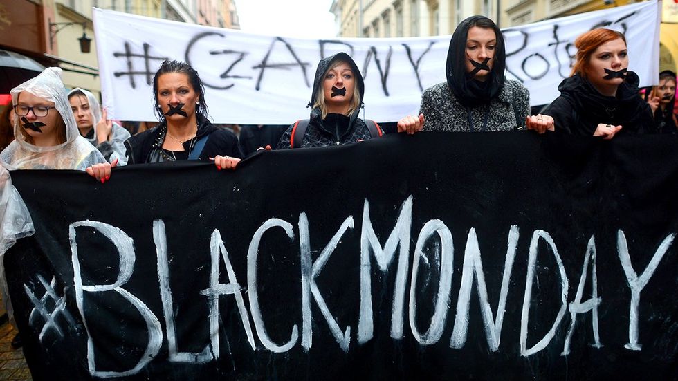 Women with banners wearing black participate in Black Monday action organized to express opposition to tightening anti abortion laws nationwide pro abortion rights protest October 2016 Castle Square Warsaw Poland